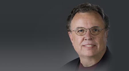 John McCafferty in burgundy outfit, professional headshot with friendly smile.