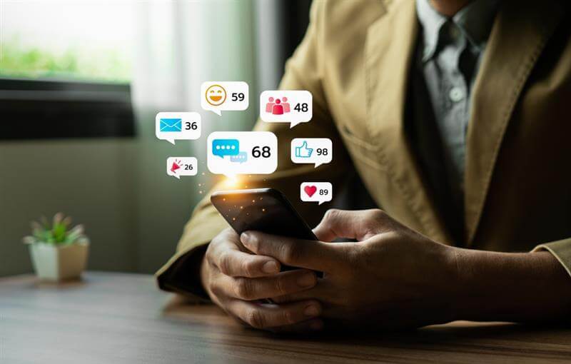 Young man using smartphone with multiple social media notifications displayed on screen.