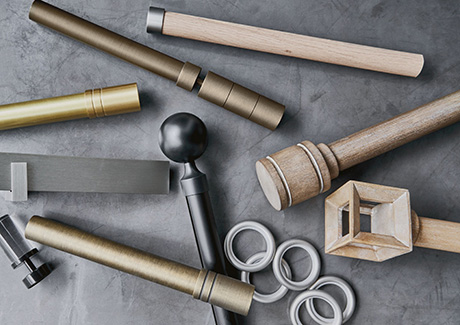 An assortment of drapery hardware pieces including rods, rings and tracks, lay decoratively on a dark grey marble-like table