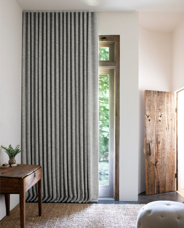 A rustic entryway featuring motorized Ripple Fold Drapery in Claude Stripe Alabaster fabric over a glass door