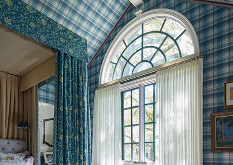 A blue patterned bedroom has curtains over arched windows made of Pinch Pleat Drapery in C.O.M. hung below the arch