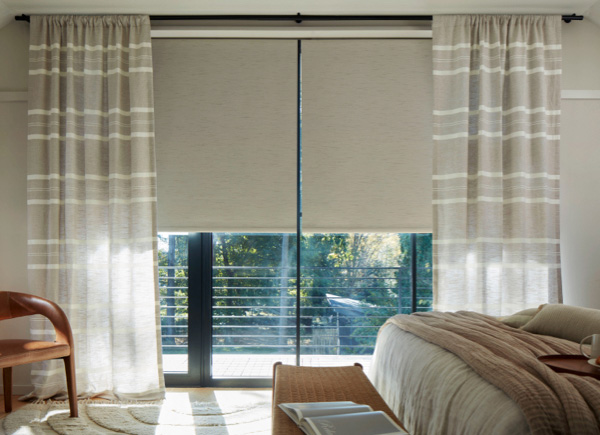Large windows featuring rod pocket drapery in shoreham stripe oatmeal in a bedroom with a white bed with a throw blanket
