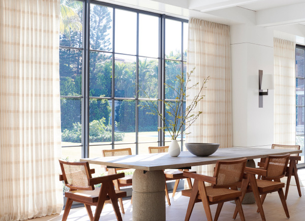 Floor to ceiling windows featuring tailored pleat drapery in lily buff in a dining room with a stone table and wood chairs