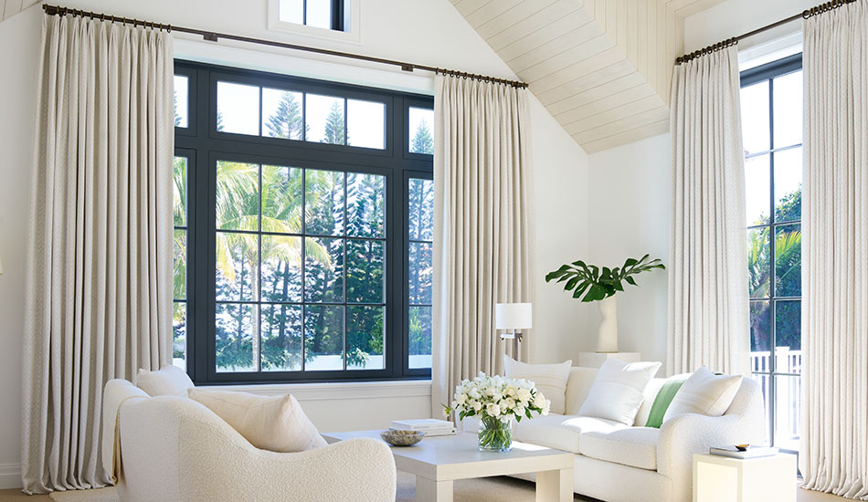 Two windows feature insulating curtains in a tailored pleat style beside a relaxing area with two couches facing one another