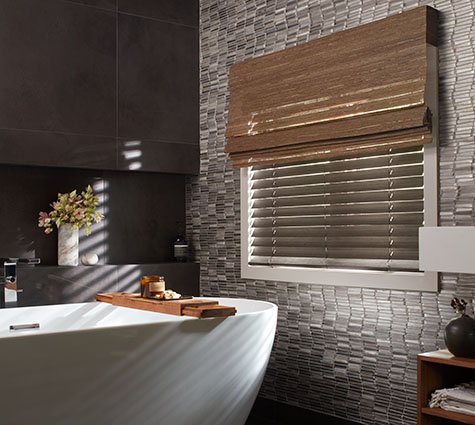 Layering styles is trendy in 2026, as seen in this bathroom's Waterfall Woven Shades over Wood Blinds