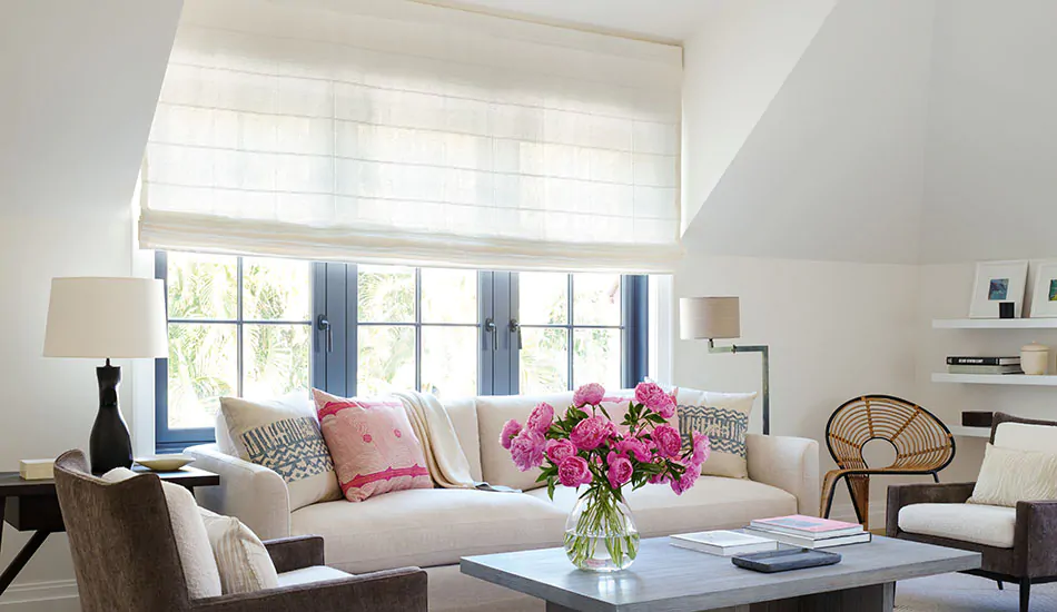 A sitting room with bright pink flowers has privacy shades in the Flat Roman Shade style made of Sankaty Stripe in Moon as light-filtering window coverings that soften natural light