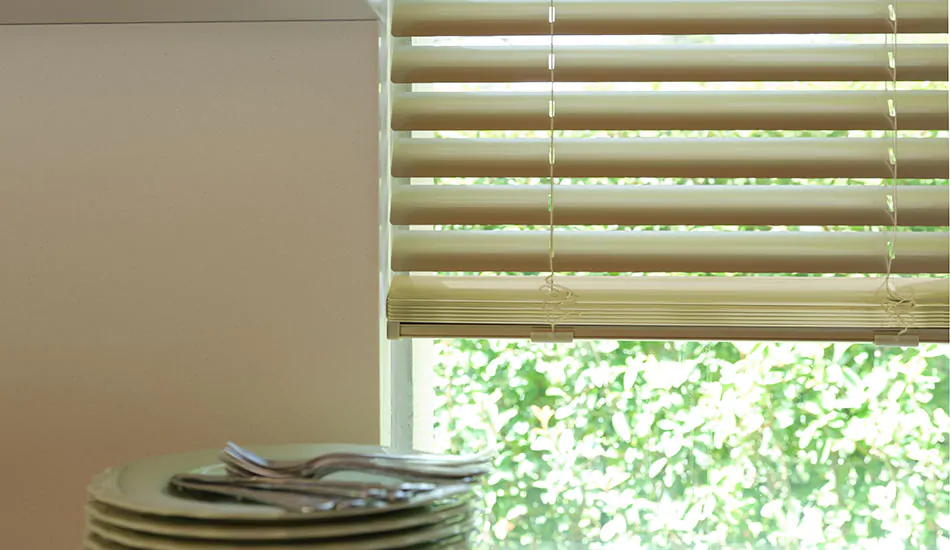 Gold champagne metal blinds used in a kitchen window next to a counter with plates are one option blinds for bay windows