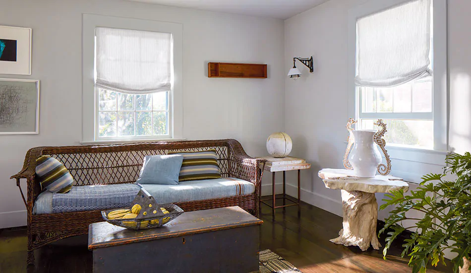Contemporary window shade treatments in a coastal inspired sitting room include relaxed Roman Shades with subtle stripes