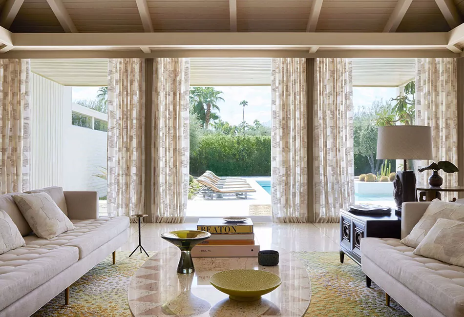 Modern boho transitional living room with Ripple Fold Drapery framing glass doors that open to a poolside outdoor space.