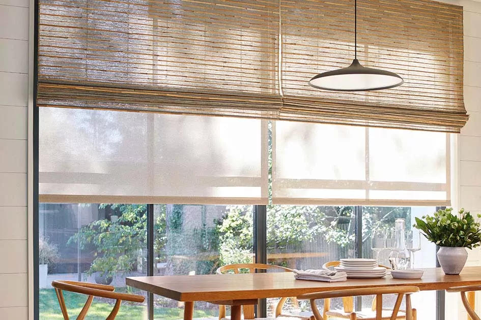 Mid century window treatments including a tan roller shade paired with a light wood toned Waterfall Woven Wood Shade in a sunlit room