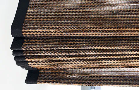 A close-up of the folds of bamboo blinds made of Del Rey in Shadow show the texture of the material and border tape in black